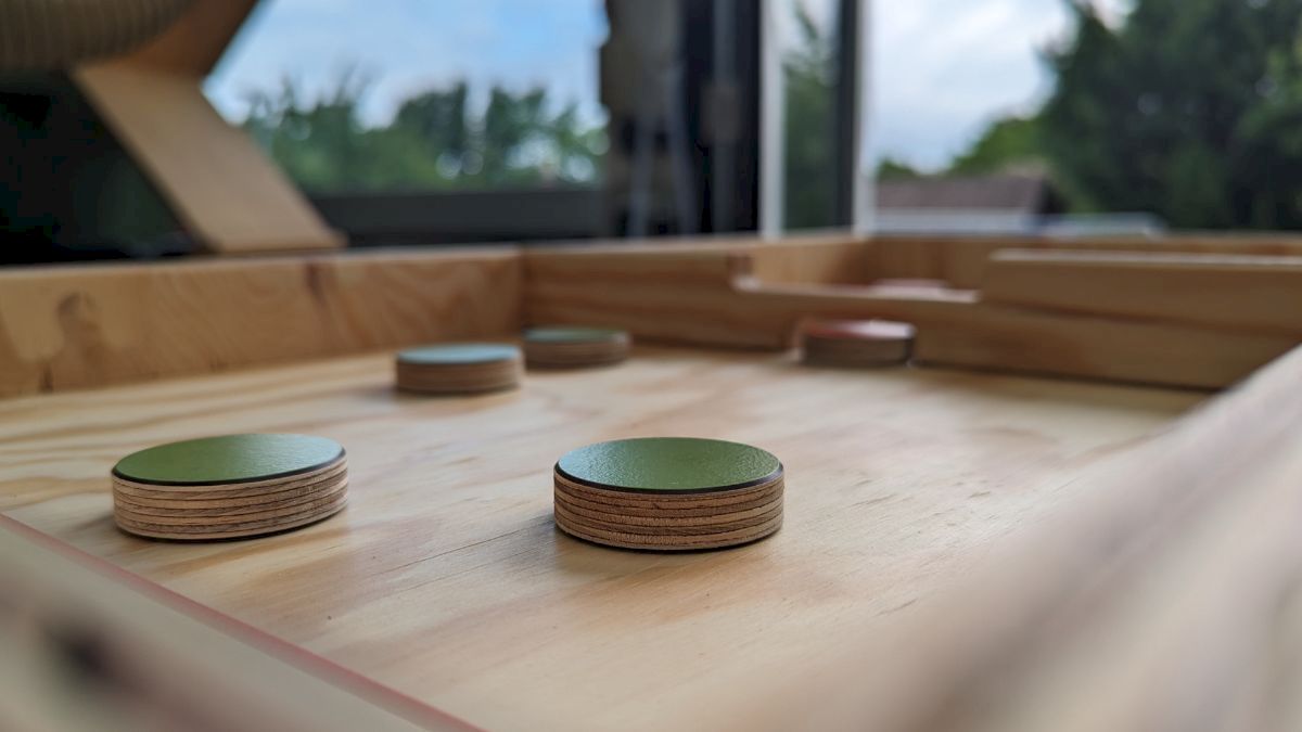 Auf dem Bild ist das Spiel "Puckspiel" aus Holz zu sehen. Es liegen verschiedene runde Holzsteine im Spielfeld.